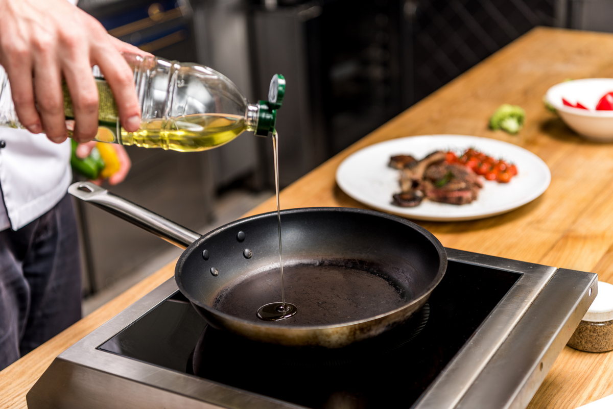 Повар добавляет растительное масло для жарки на сковороду