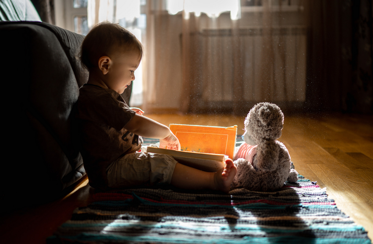 Мальчик читает книжку плюшевому медвежонку