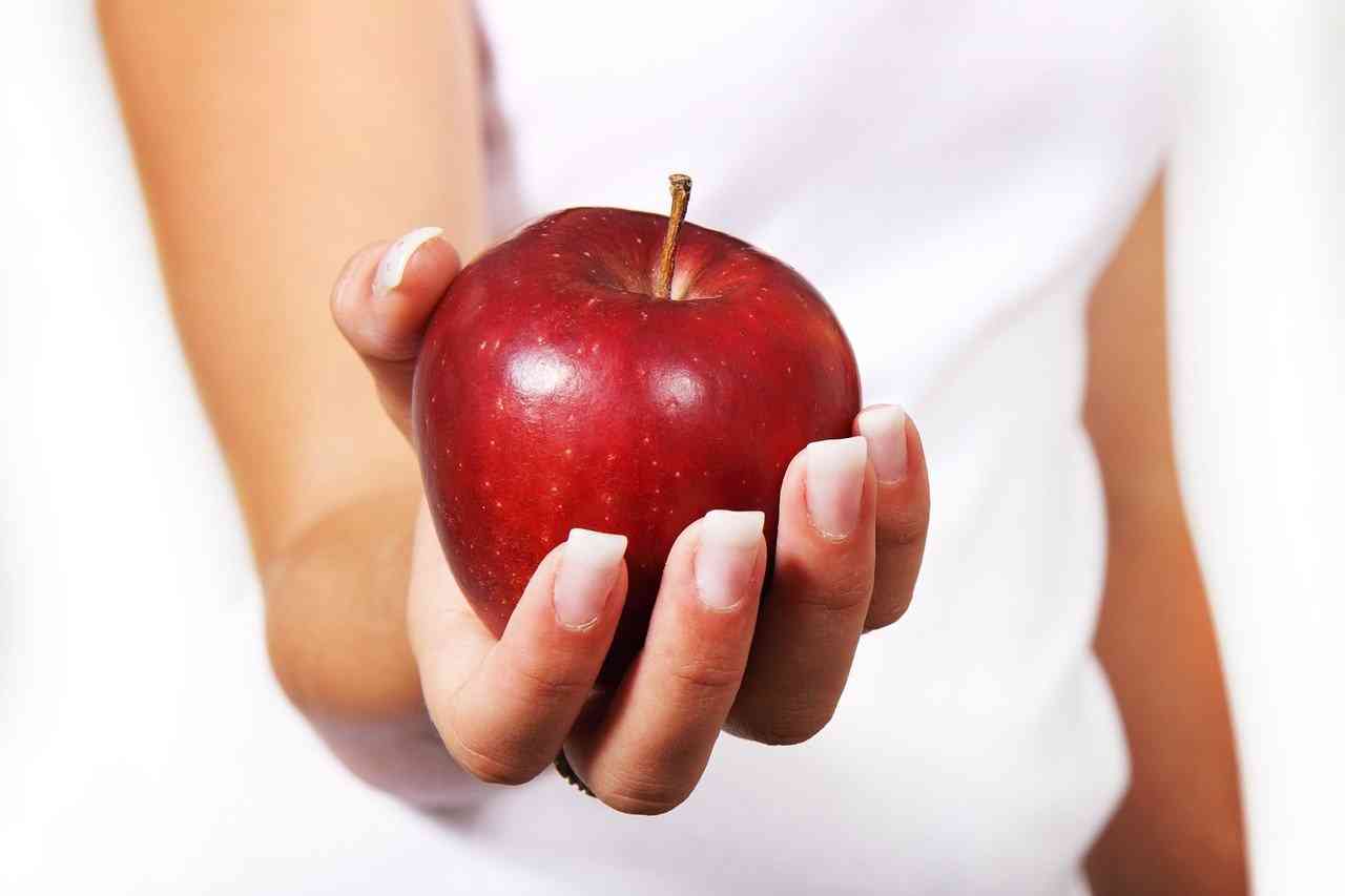 Девушка в белом держит в руках красное яблоко