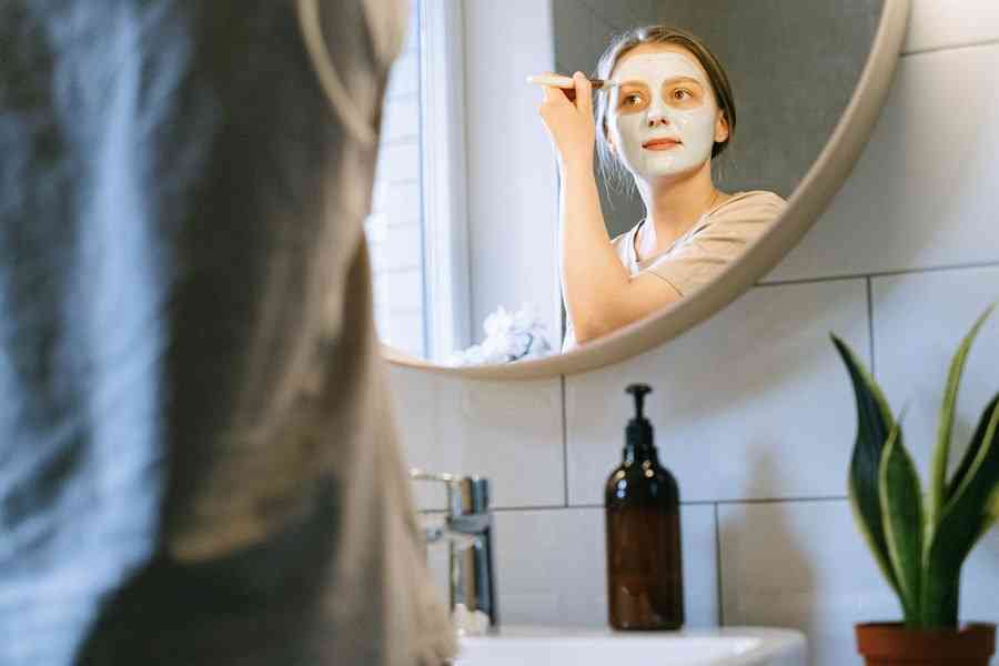 Девушка наносит белую косметическую маску на лицо в ванной