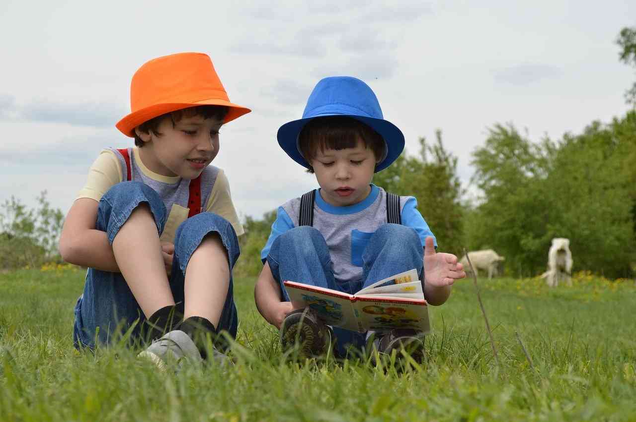 Два мальчика в красивых костюмчиках и шляпах сидят на траве и читают книгу