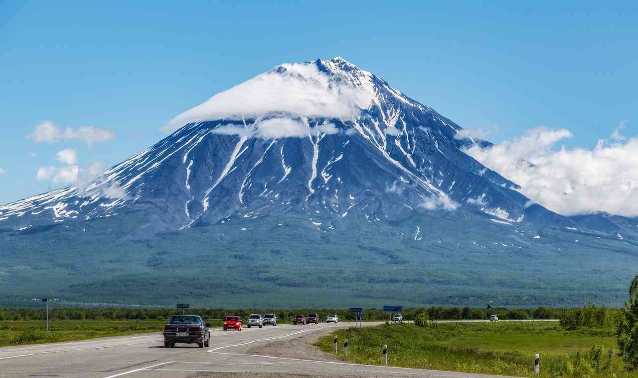 Машины едут на фоне вулкана на Камчатке