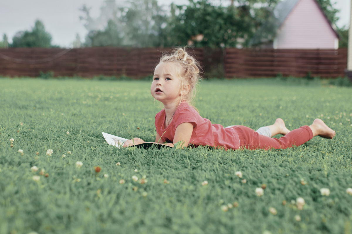 Девочка лежит на траве и читает книгу