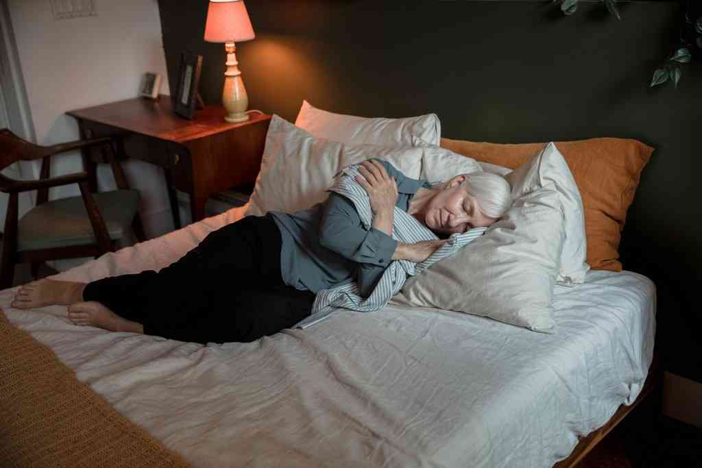 Женщина в одежде лежит на заправленной кровати в куче подушек