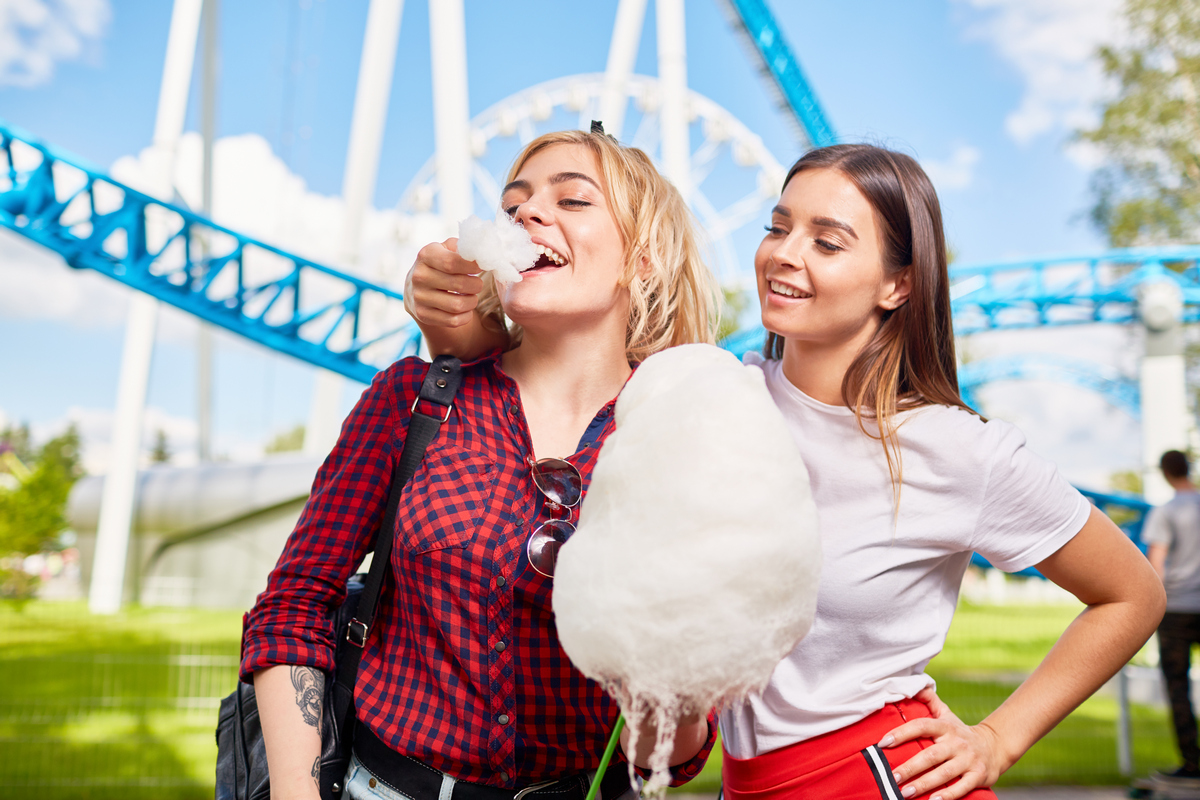 две симпатичные девушки едят сладкую вату в парке аттракционов