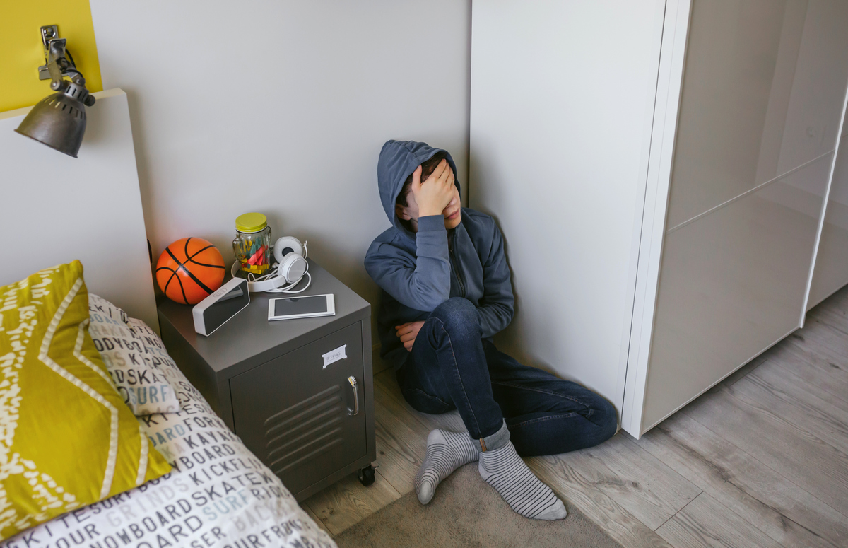 Подросток в стрессе сидит на полу в комнате