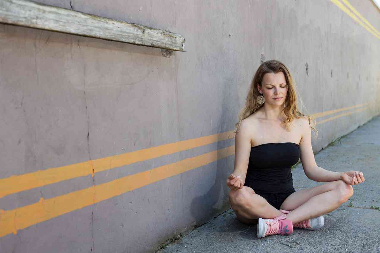 Женщина медитирует на асфальте возле бетонной стены