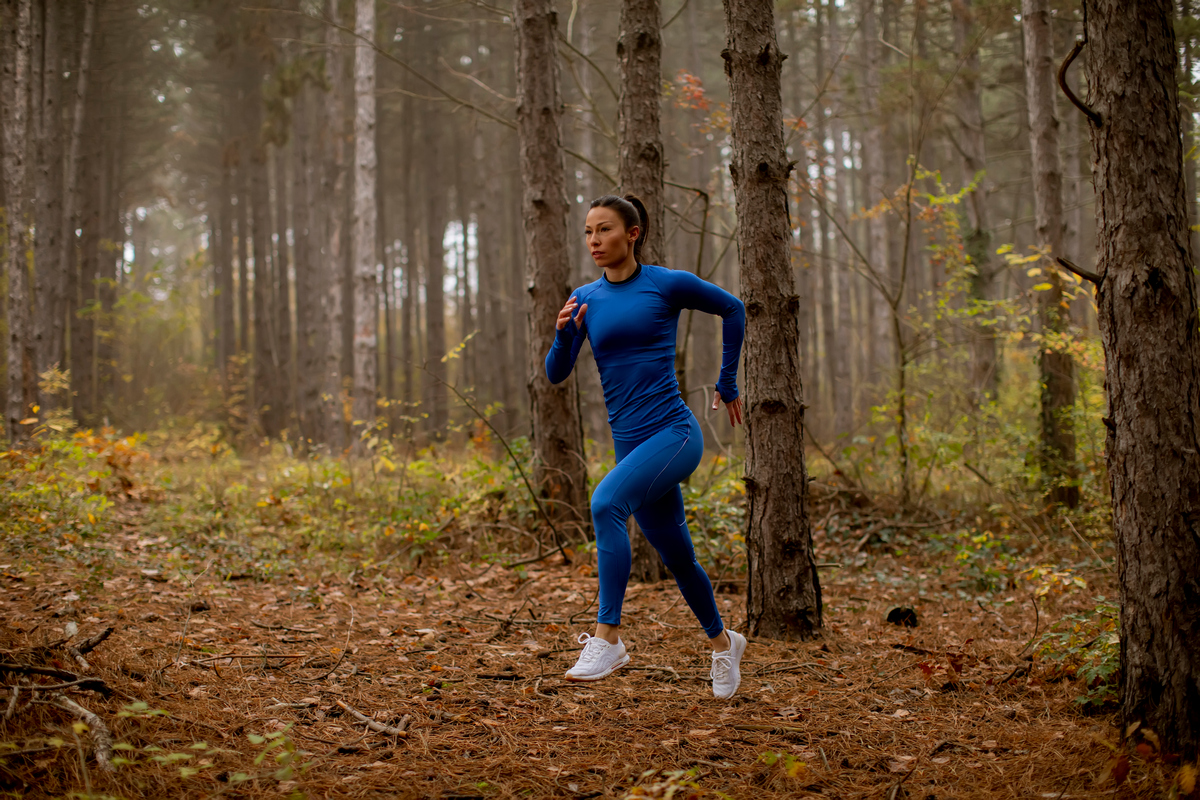 Женщина в синем спортивном костюме бежит по лесу