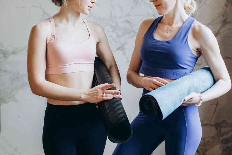 Две женщины в спортивной одежде стоят с ковриками для йоги