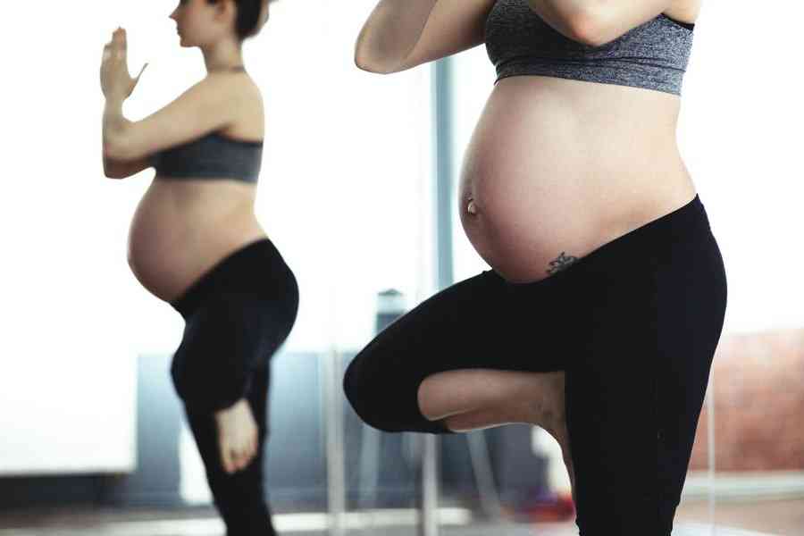 Беременная женщина занимается около зеркала йогой