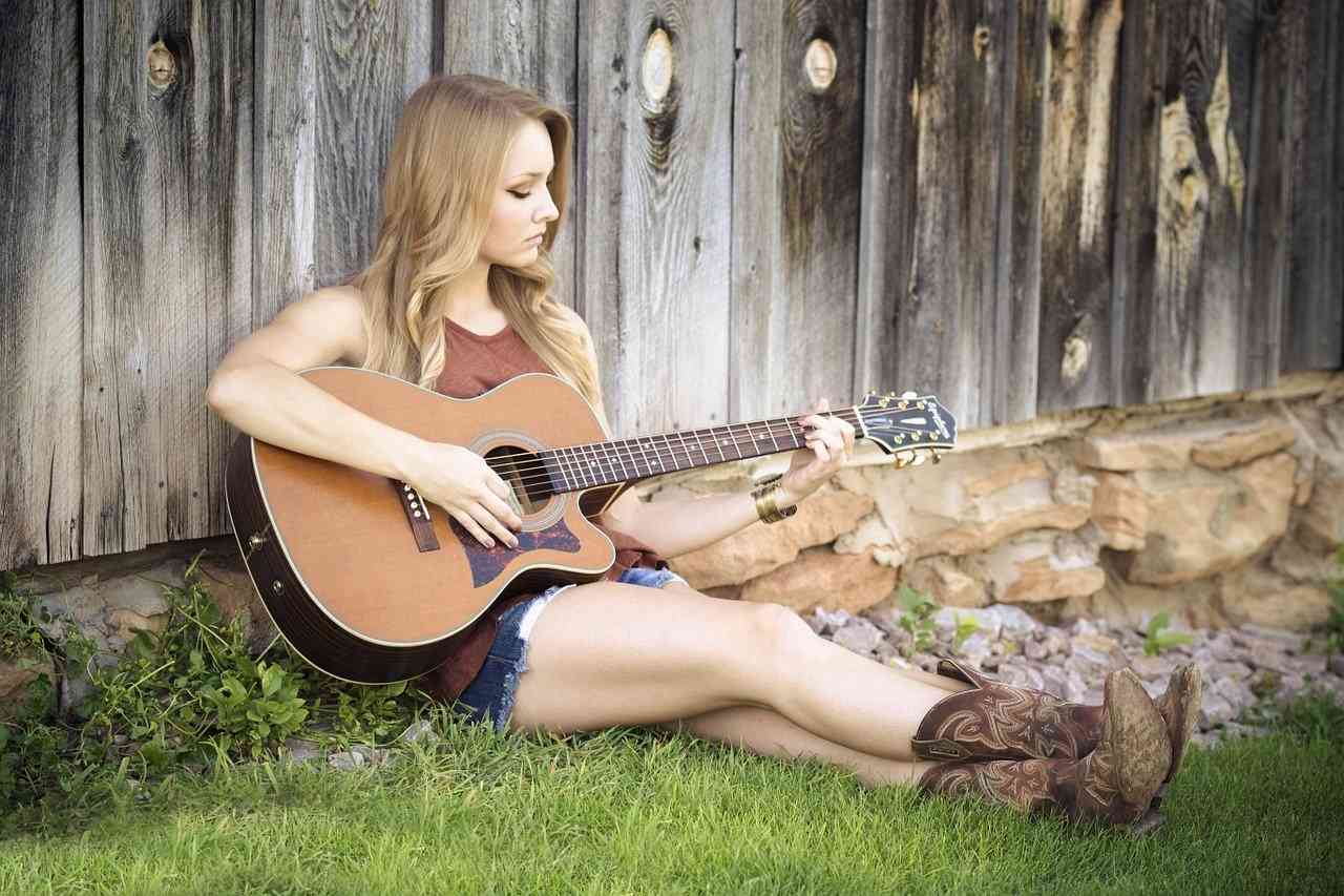 Девушка сидит на траве прислонившись к забору и играет на гитаре