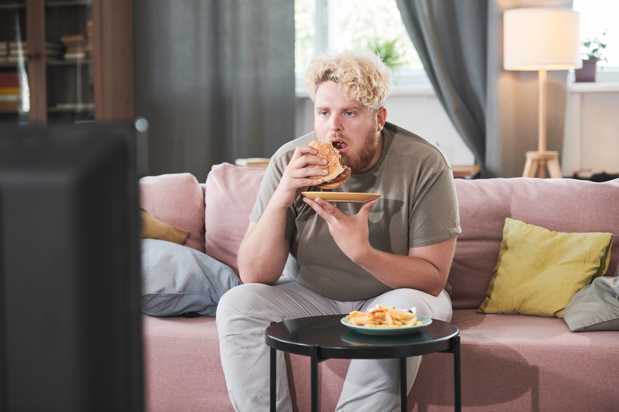 Мужчина с гамбургером за просмотром ТВ